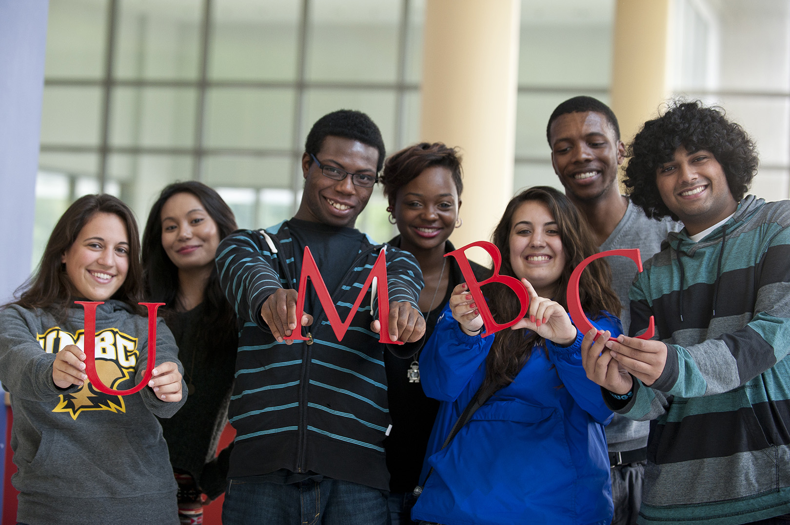 A diverse group of seven students standing close together happily and holding up the letters UMBC.