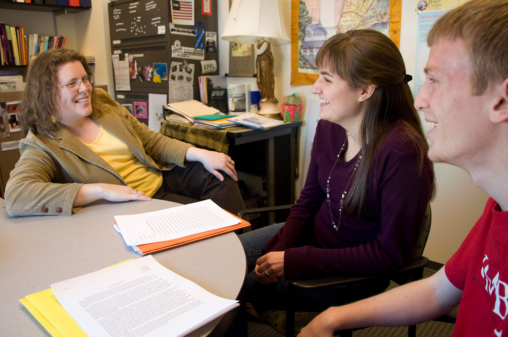 A professor sitting comfortably and laughing with two students in an office.