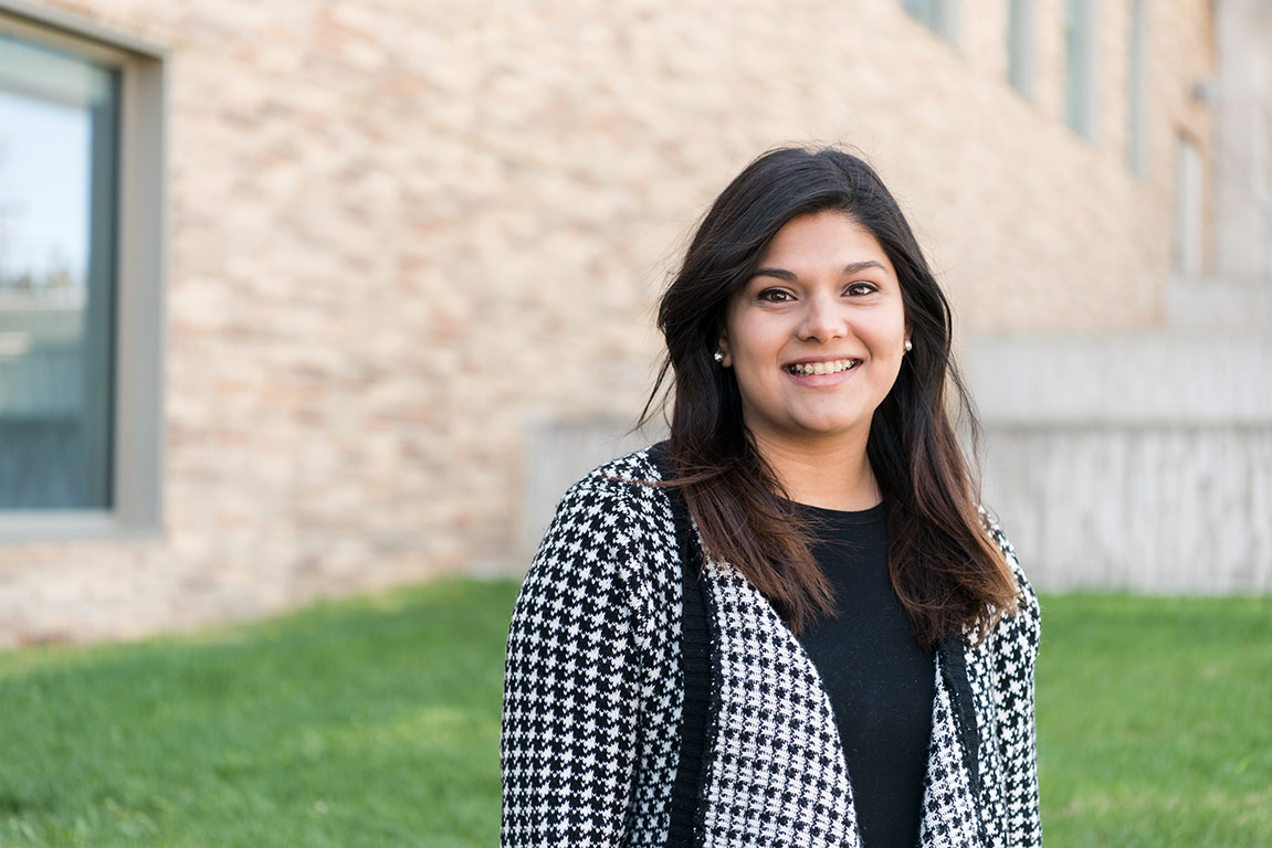 Summer, dressed professionally and smiling outside an academic building near the quad.