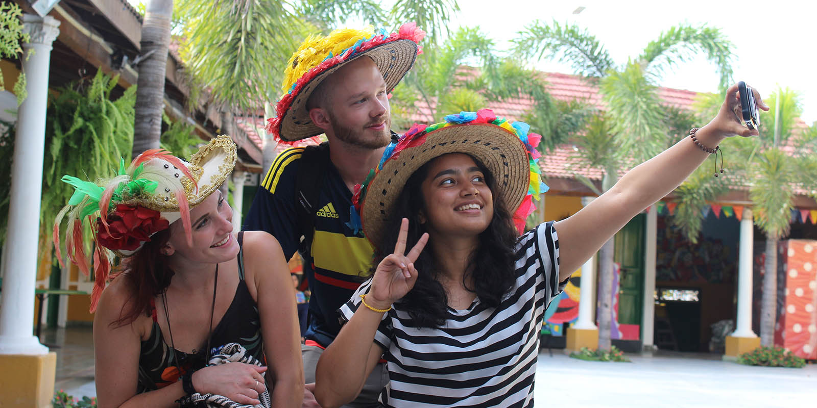 Students in festive hats taking a selfie near palm trees.